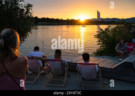 Junge Menschen sitzen am Ufer der Neuen Donau am Copa Beach bei Sonnenuntergang, Wien, Österreich Stockfoto