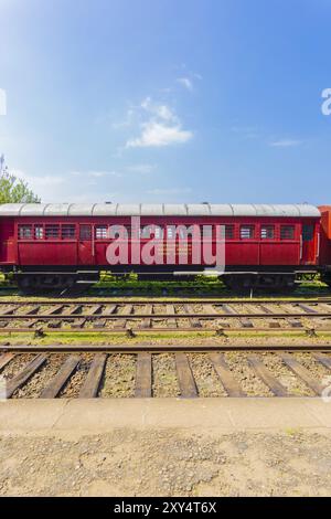 Seitenansicht eines alten stationären roten Personenwagens, der an einem Tag mit blauem Himmel auf Bahngleisen, Teil der Sri Lanka Railways, geparkt ist. Vertikal Stockfoto