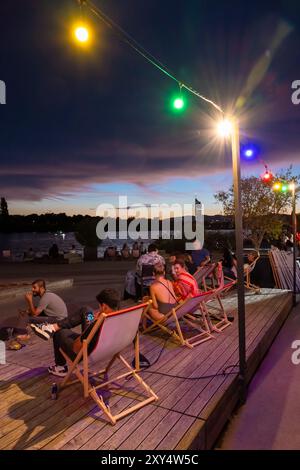 Junge Leute, die am Ufer der Neuen Donau sitzen, in der Bar D'arepa am Copa Beach in der Abenddämmerung, Wien, Österreich Stockfoto