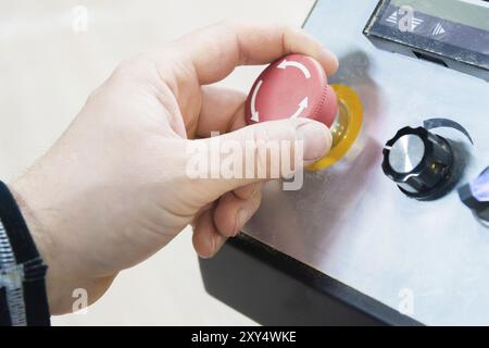 Nahaufnahme der Hand eines Mannes auf einer roten Taste auf dem Bedienfeld. Not-aus oder Start der Anlage und Produktion Stockfoto