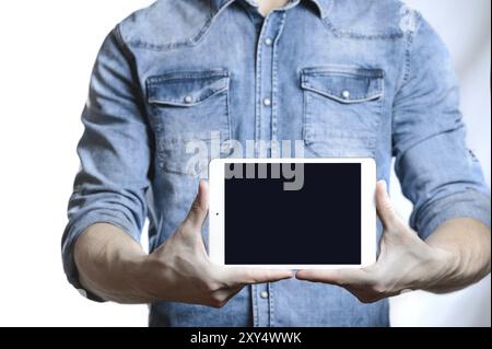 Lässiger Mann in Denim-Hemd, der digitalen Tablet-Computer-Bildschirm in den Händen zeigt. Isoliert auf weiß. Beschneidungspfad für die Anzeige enthalten. Er zeigt mit einem Finger A Stockfoto