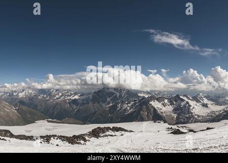 Ein dunkelblauer Himmel mit Wolken auf den felsigen Gipfeln von Bergen, die mit Gletschern und Schnee im Kaukasus bedeckt sind Stockfoto