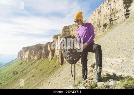 Ein Mädchen mit Sonnenbrille legt einen Rucksack auf die Natur vor einem Hintergrund epischer Felsen, die sich auf eine Wanderung mit Klettern vorbereiten Stockfoto