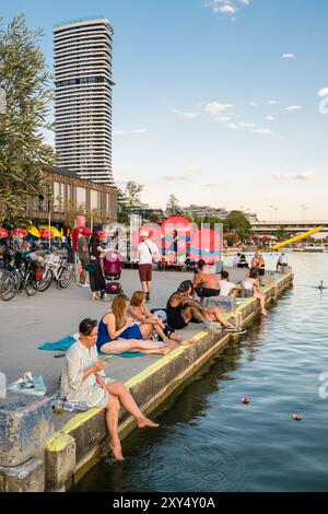 Menschen, die während des Sonnenuntergangs am Copa Beach am Ufer der Neuen Donau sitzen und einem Musiker lauschen, Wien, Österreich Stockfoto