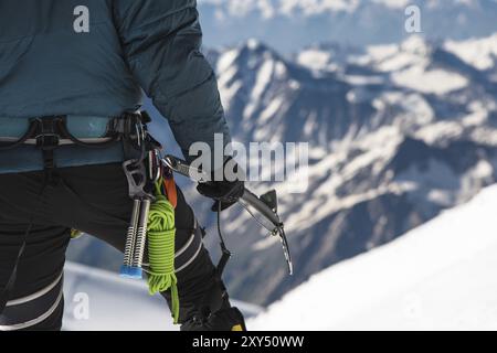 Nahaufnahme Ein junger Kletterer hält in der Hand eine Eisaxt, die auf dem Gipfel hoch in den Bergen vor dem Hintergrund des schneebedeckten Kaukasiens steht Stockfoto