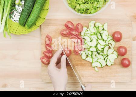 Zarte Frauenhände schneiden zu Hause ein großes Messer mit Tomaten auf ein Viertel auf einem Holzbrett. Wohnküche. Gesunde Ernährung. Das Konzept von ve Stockfoto