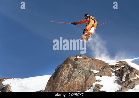 Ein professioneller Skifahrer macht einen Sprung von einer hohen Klippe gegen den blauen Himmel und hinterlässt eine Spur aus Schneepulver in den Bergen. Foto von den Pisten o Stockfoto