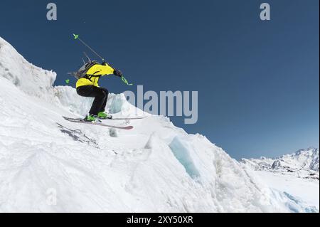Ein Skifahrer in voller Sportausrüstung springt von der Spitze des Gletschers in den Abgrund vor dem Hintergrund des blauen Himmels und der kaukasischen Schneedecke Stockfoto