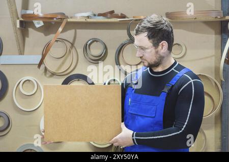 Der Hersteller von Möbeln in Spezialkleidung und Schutzbrille hält am Arbeitsplatz eine leere Platte für den Text. Handwerkliche Herstellung von Möbeln Stockfoto