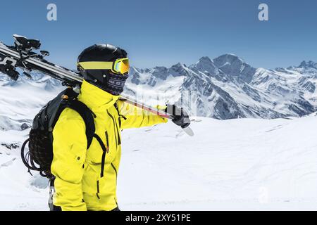 Ein großes Porträt eines Skifahrers in Schutzhelm und Brille ist eine Maske und ein Schal mit Skiern auf der Schulter in den schneebedeckten Bergen des Kauca Stockfoto