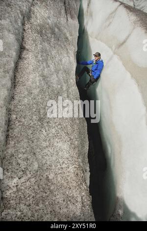 Ein freier Kletterer ohne Versicherung mit zwei Eisachsen steigt aus einem Riss im Gletscher auf. Freies Klettern ohne Seile Stockfoto