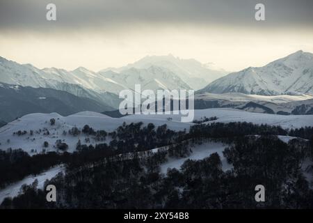 Blick auf den kaukasischen Bergrücken mit Wolken, die auf den Gipfeln von Bergen hängen, die mit Schnee bedeckt sind, fotografiert vom Hang des Vulkans Elbrus Stockfoto