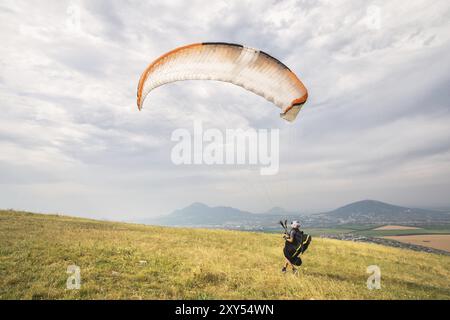 Ein Mann Gleitschirm, der vom Rand des Berges mit Feldern im Hintergrund abheben. Gleitschirmfliegen Stockfoto