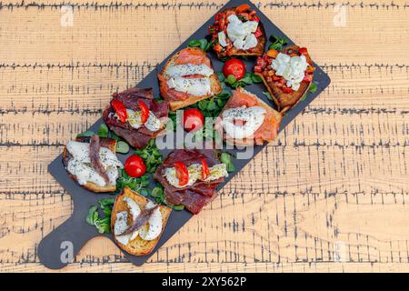 Köstliche Auswahl an italienischen Bruschetta-Vorspeisen auf dunkler Servierplatte. Mit Belägen wie Mozzarella, Tomaten, Schinken und Lachs. Pro Stockfoto