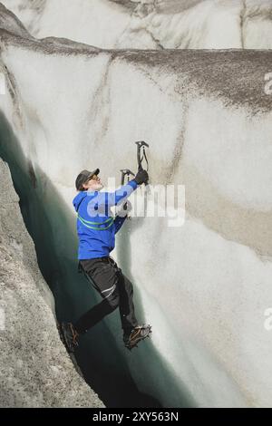 Ein freier Kletterer ohne Versicherung mit zwei Eisachsen steigt aus einem Riss im Gletscher auf. Freies Klettern ohne Seile Stockfoto