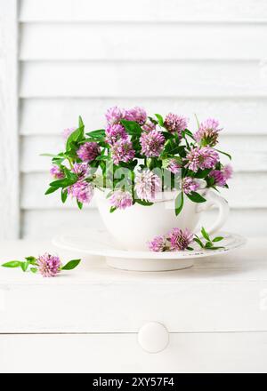 Wunderschöner Blumenstrauß aus rotem Kleeblatt in einer Vintage-Teetasse. Rustikales Stillleben mit Wildblumen. (Trifolium pratense). Selektiver Weichfokus. Stockfoto