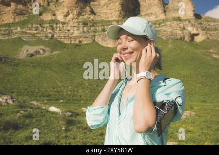 Fitness-Läuferin schließt die Augen und hört Musik über die Natur. Porträt eines schönen Mädchens, das Kopfhörer-Ohrstöpsel und Laufkappe für Sonne trägt Stockfoto