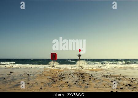 Rettungsschirm und Mast mit roter Flagge am Strand, wenn die Flut steigt Stockfoto