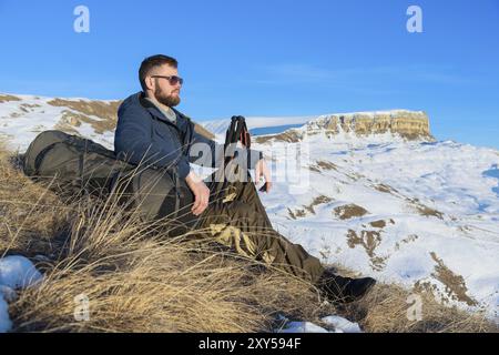 Porträt des ruhigen Hipster-Reisenden mit Bart in der Sonnenbrille sitzt auf der Natur. Ein Mann wandert in den Bergen mit Rucksack und skandinavischem Wa Stockfoto