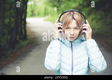 Porträt eines attraktiven Sportmädchens in einer leichten Daunenjacke, die bluetooth-Kopfhörer mit Musik oder Naturgeräuschen anzieht Stockfoto