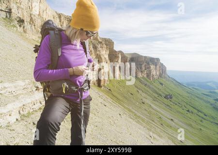 Ein Tourist in Sonnenbrille legt einen Rucksack in die Natur vor dem Hintergrund epischer Felsen, die sich auf Trekking mit Klettern vorbereiten. Die Wanderer fesselt die Stockfoto