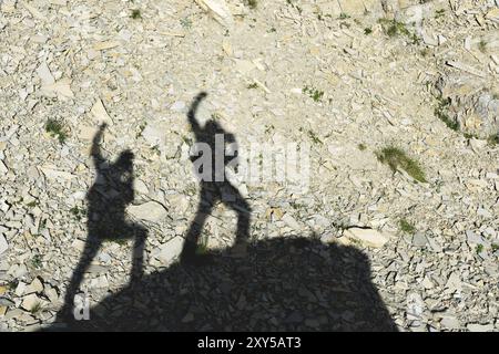 Zwei Schatten von Fotografen auf der Erde, die mit erhobenen Händen nach Sieg und Erfolg schreien. Silhouetten von zwei Personen, die uph laufen Stockfoto