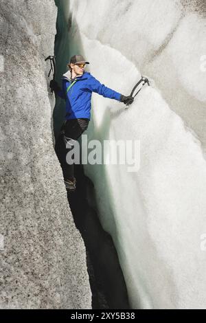 Ein freier Kletterer ohne Versicherung mit zwei Eisachsen steigt aus einem Riss im Gletscher auf. Freies Klettern ohne Seile Stockfoto