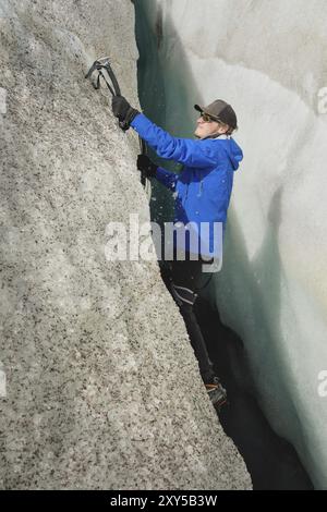 Ein freier Kletterer ohne Versicherung mit zwei Eisachsen steigt aus einem Riss im Gletscher auf. Freies Klettern ohne Seile Stockfoto