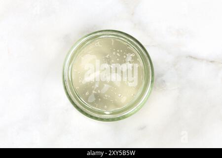 Ein Glas Glas mit Aloe vera Gel, Schuß von oben auf weißem Marmor Hintergrund mit Kopie Raum Stockfoto