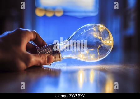 Hände halten eine LED-Glühbirne über dem Holzboden. Symbol für Ideen und Innovation. Fenster und Licht im unscharfen Hintergrund Stockfoto