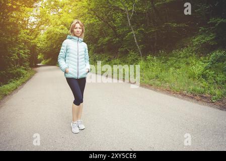 Porträt eines attraktiven Sportmädchens in einer leichten Daunenjacke, die bluetooth-Kopfhörer mit Musik oder Naturgeräuschen anzieht Stockfoto