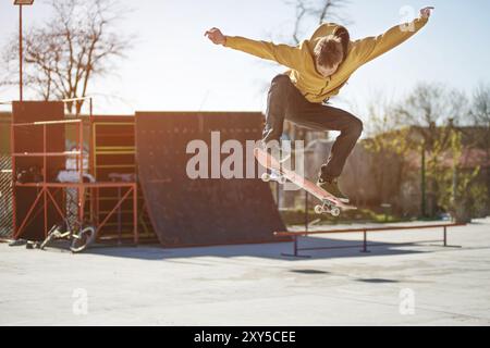 Ein Teenager-Skateboarder macht einen ollie-Trick in einem Skatepark am Stadtrand vor dem Hintergrund von Kickern Stockfoto