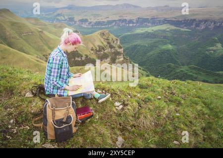 Mädchen mit mehrfarbigem Haar, das auf einer Naturlesekarte sitzt und einen Kompass in der Hand hält. Das Konzept der Navigation in der Suche und Tourismus i Stockfoto