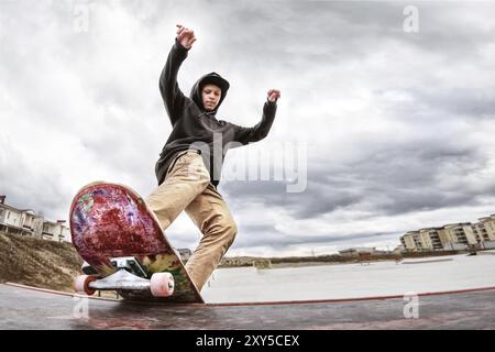 Teenager Skater in Hoodie Sweatshirt und Jeans gleiten über ein Geländer auf einem Skateboard in einem Skatepark, Weitwinkel Stockfoto