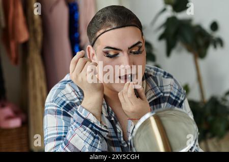 Eine schwule Person in stilvoller Kleidung trägt Lippenstifte, während sie in einen Spiegel blickt. Stockfoto