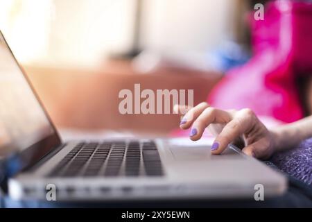 Mädchen mit violetten Fingernägeln benutzt ihren Laptop zu Hause auf der Couch Stockfoto