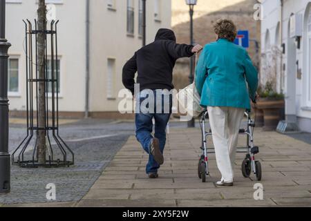 Ein Mann schnappt sich die Handtasche einer Seniorin von der Schulter, als sie vorbeikommt. Rückansicht Stockfoto