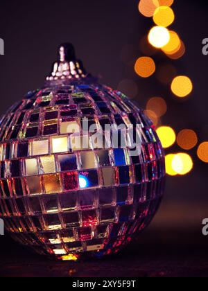 Nahaufnahme von einem bunten disco Weihnachtskugel auf einem Holztisch, verschwommenes Weihnachtsbaumbeleuchtungen im Hintergrund, schönes Bokeh Stockfoto