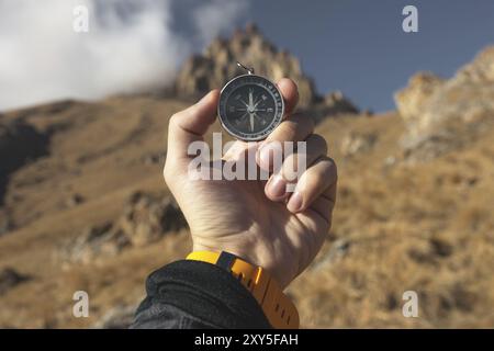 Ein männlicher Wanderer sucht im Herbst eine Richtung mit einem magnetischen Kompass in den Bergen. POV-Aufnahme. Die Hand eines Mannes mit einem Uhrenarmband Stockfoto