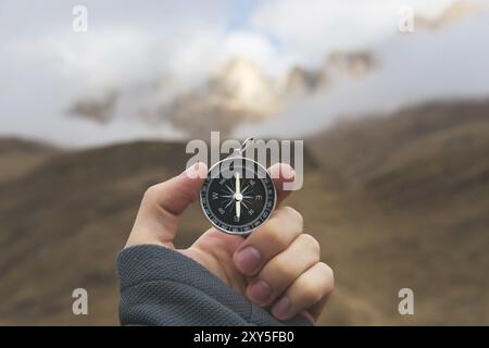 Ein männlicher Wanderer sucht im Herbst eine Richtung mit einem magnetischen Kompass in den Bergen. POV-Aufnahme. Die Hand eines Mannes mit einem Uhrenarmband Stockfoto