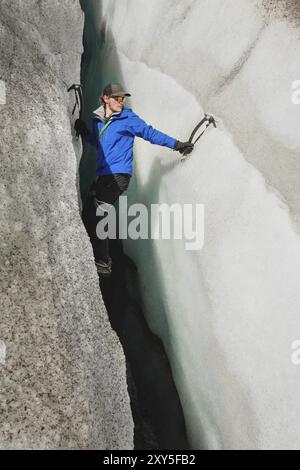 Ein freier Kletterer ohne Versicherung mit zwei Eisachsen steigt aus einem Riss im Gletscher auf. Freies Klettern ohne Seile Stockfoto