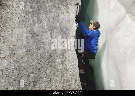 Ein freier Kletterer ohne Versicherung mit zwei Eisachsen steigt aus einem Riss im Gletscher auf. Freies Klettern ohne Seile Stockfoto