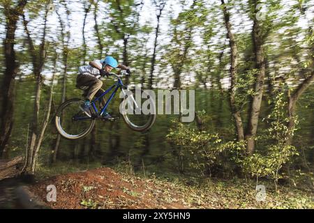 Ein junger Fahrer mit Helm fliegt auf einem Fahrrad, nachdem er von einem Hochkicker auf einem Waldradweg gesprungen ist Stockfoto