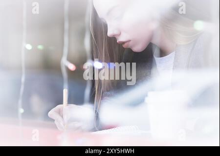 Porträt einer attraktiven jungen Journalistin mit Stift und Notizblock im Café hinter dem Schaufenster. Kontrastfreie Sicht durch Glasreflexion Stockfoto