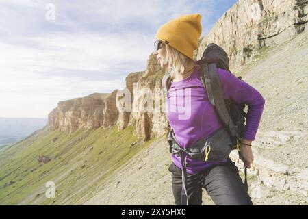 Ein Tourist in Sonnenbrille legt einen Rucksack in die Natur vor dem Hintergrund epischer Felsen, die sich auf Trekking mit Klettern vorbereiten. Die Wanderer fesselt die Stockfoto