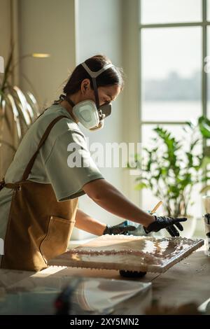 Nahaufnahme einer Künstlerin, die Epoxidharz mit Handschuhen aufträgt, in der Nahaufnahme des Kunststudios. Flüssige Kunst. Stockfoto