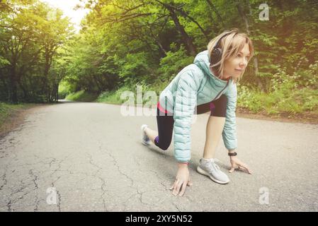 Athletische Frau läuft auf dem Land Straße. Fitness-Lauferin in bereit Startlinie Pose im Sommer Sprint Herausforderung Stockfoto