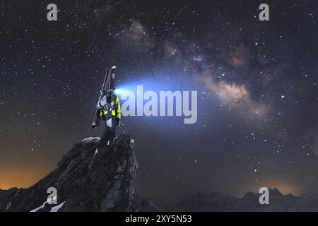 Nachtlandschaft. Ein professioneller Skiläufer mit Rucksack und Skiern steht auf einem Felsen in den Bergen und glänzt mit einer Stirnlampe im Milky W Stockfoto