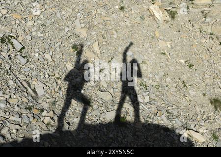 Zwei Schatten von Fotografen auf der Erde, die mit erhobenen Händen nach Sieg und Erfolg schreien. Silhouetten von zwei Personen, die uph laufen Stockfoto