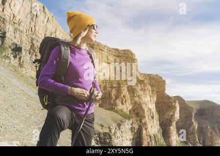 Ein Tourist in Sonnenbrille legt einen Rucksack in die Natur vor dem Hintergrund epischer Felsen, die sich auf Trekking mit Klettern vorbereiten. Die Wanderer fesselt die Stockfoto